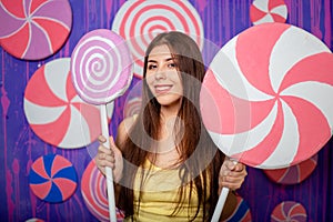 A beautiful, young woman with a big toy candy in her hands, stands on an abstract violet-blue background of sweets and lollipops.