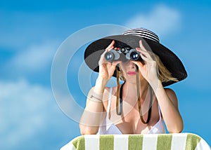 Beautiful young woman in bikini looking through binoculars at the tropical beach