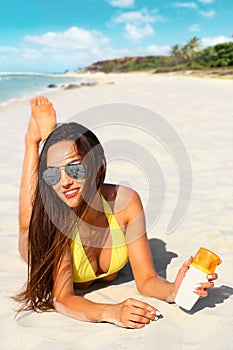 Beautiful young woman in bikini with protective cream in the hand on the beach under the sun