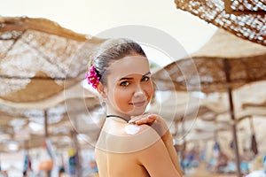 Beautiful young woman in bikini smear protective cream on the skin on the beach under the sun.