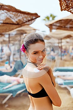 Beautiful young woman in bikini smear protective cream on the skin on the beach under the sun.