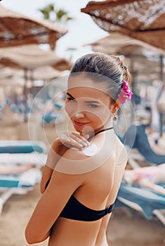 Beautiful young woman in bikini smear protective cream on the skin on the beach under the sun.