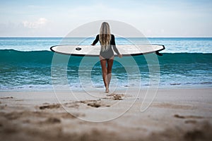 Beautiful young woman in bikini with surf board at beach of tropical island.