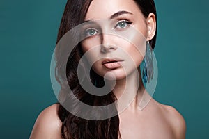 Beautiful young woman with bird feathers earrings over color background