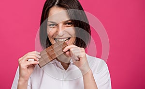 Beautiful young woman bites a bar of chocolate.