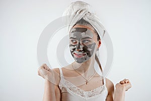 Beautiful young woman with black clay facial mask for perfect fresh clean skin isolated on white