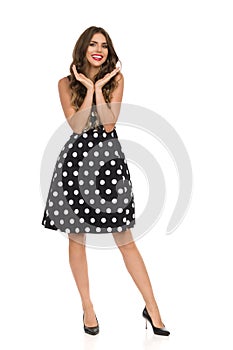 Beautiful Young Woman In Black Cocktail Dress In Polka Dots Is Holding Head In Hands And Smiling