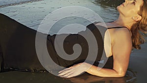 Beautiful young woman in black dress lying down in water