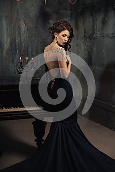 Beautiful young woman in black dress next to a piano with candelabra candles and wine, dark dramatic atmosphere of the castle.