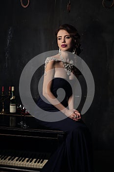 Beautiful young woman in black dress next to a piano with candelabra candles and wine, dark dramatic atmosphere of the castle.