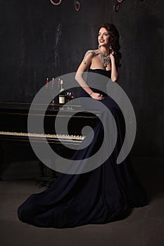 Beautiful young woman in black dress next to a piano with candelabra candles and wine, dark dramatic atmosphere of the castle.