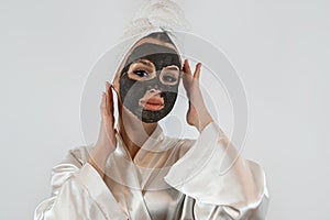 Beautiful young woman with a black mud or clay mask for the face isolated on white