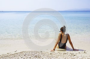 Beautiful young woman in a black swimsuit sits on the sand of a beach in Makarska, Croatia.