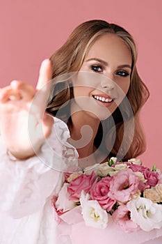 Beautiful young woman with blond curly hair in elegant clothes posing with bouquet of spring flowers