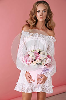 Beautiful young woman with blond curly hair in elegant clothes posing with bouquet of spring flowers