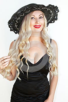 Beautiful young woman blonde in black dress and hat with decollete. photo