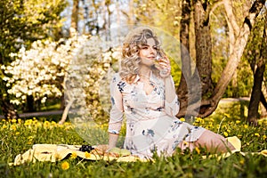 Beautiful young woman with blonde hair in straw hat drinks wine in the garden