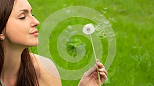 Beautiful young woman blowing on dandelion