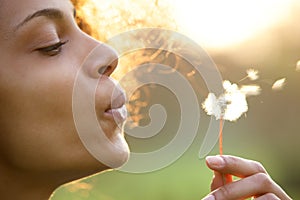 Beautiful young woman blowing dandelion flower