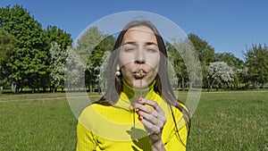 Beautiful young woman blowing a dandelion. Girl with dandelion in hand. Allergic to pollen of flowers. Spring allergy.