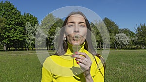 Beautiful young woman blowing a dandelion. Girl with dandelion in hand. Allergic to pollen of flowers. Spring allergy