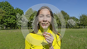 Beautiful young woman blowing a dandelion. Girl with dandelion in hand. Allergic to pollen of flowers. Spring allergy