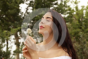 Beautiful young woman blowing dandelion in park. Allergy free concept
