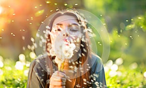 Beautiful young woman blowing dandelions