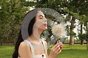 Beautiful young woman blowing large dandelion in park. Allergy free concept