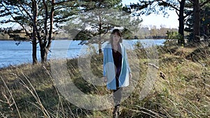 Beautiful young woman in blue coat walking down path in autumn forest in windy weather