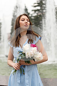 A beautiful young woman in a blue dress with a bouquet of peonies