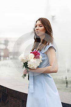 A beautiful young woman in a blue dress with a bouquet of peonies