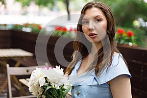 A beautiful young woman in a blue dress with a bouquet of peonies