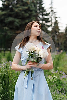 A beautiful young woman in a blue dress with a bouquet of peonies