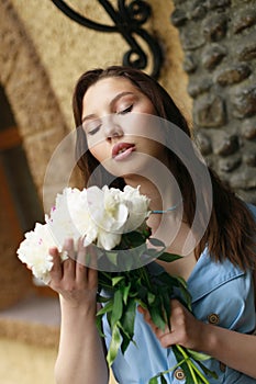 A beautiful young woman in a blue dress with a bouquet of peonies