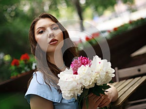 A beautiful young woman in a blue dress with a bouquet of peonies