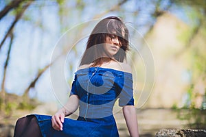 Beautiful young woman in blue dress posing in front of camera on nature background in forest.