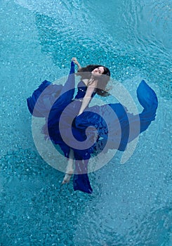 Beautiful young woman in blue evening dress floating weightlessly elegant in the water