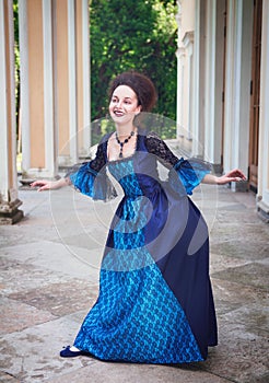 Beautiful young woman in blue medieval dress doing curtsey