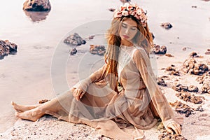 Beautiful young woman in boho dress and wreath on the beach at sunset