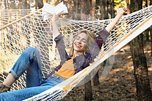 Beautiful young woman with book relaxing in hammock outdoors on summer day