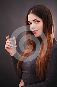 Beautiful young woman with bottle of perfume on dark background, closeup