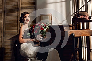 Beautiful young woman bride with a huge bouquet of red roses sits in a room with antique furniture