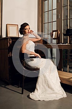 Beautiful young woman bride sitting in a room with antique furniture dressed in a white dress