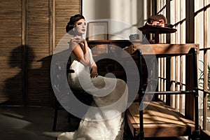 Beautiful young woman bride sitting in a room with antique furniture dressed in a white dress