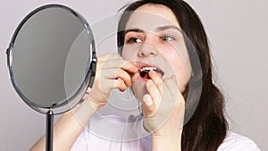 A beautiful young woman brushes her teeth with flossing in front of a mirror. Oral hygiene and dental care, prevention