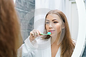 A beautiful young woman brushes her teeth and looks in the mirror