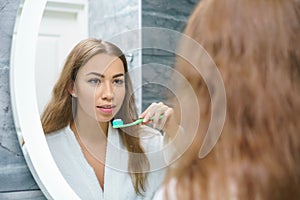 A beautiful young woman brushes her teeth and looks in the mirror