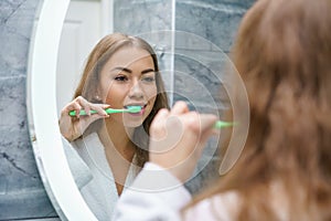 A beautiful young woman brushes her teeth and looks in the mirror