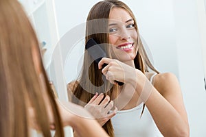 Beautiful young woman brushing her long hair in front of her mirror.